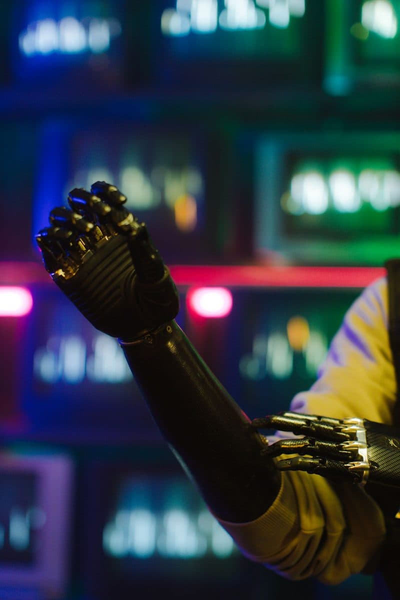 A bionic robotic arm silhouetted against colourful neon light
