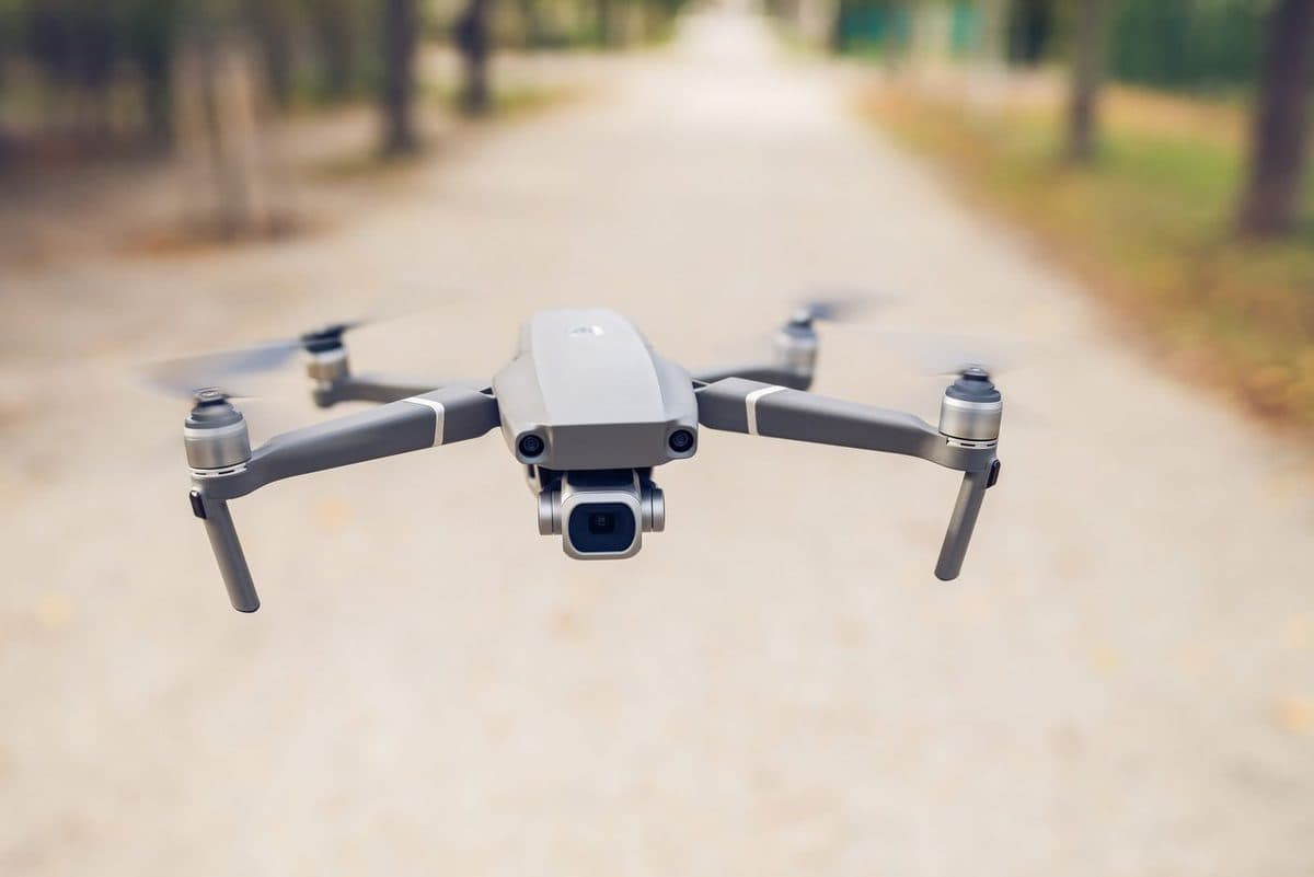 A sleek camera drone hovering along a tree-lined path