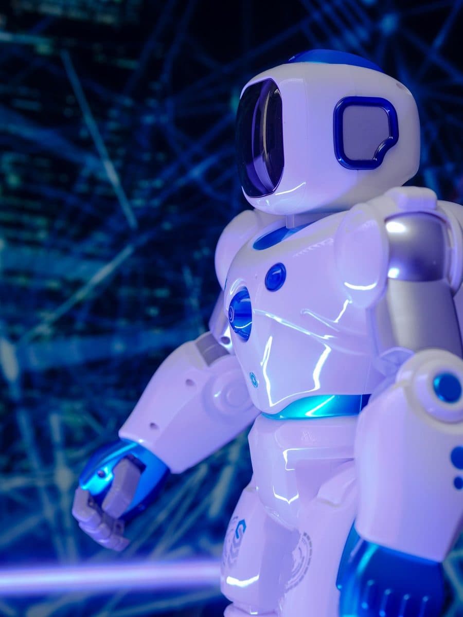 A glossy white-and-blue humanoid robot lit against a dark grid backdrop