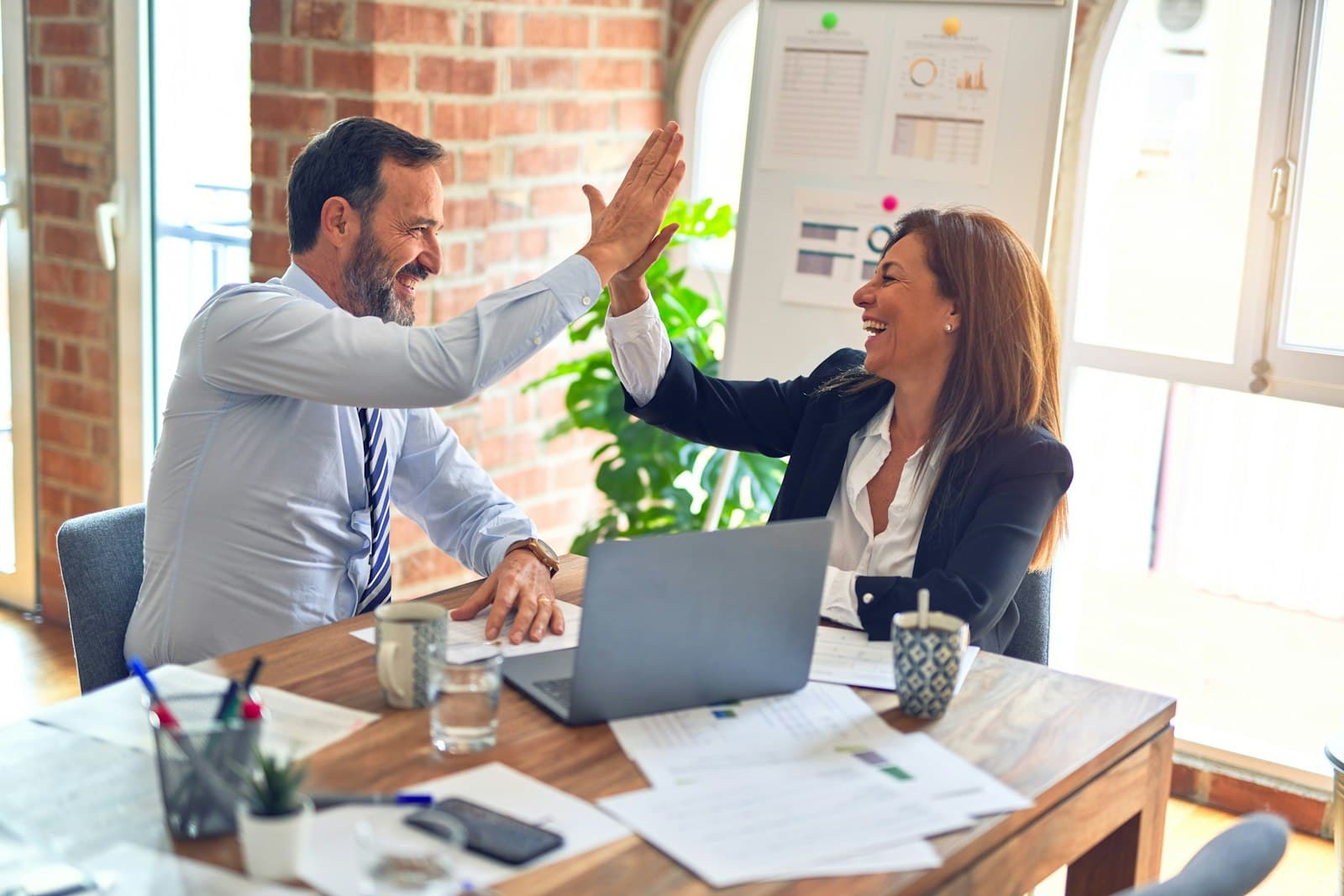 Two colleagues high-fiving at their desk after a win