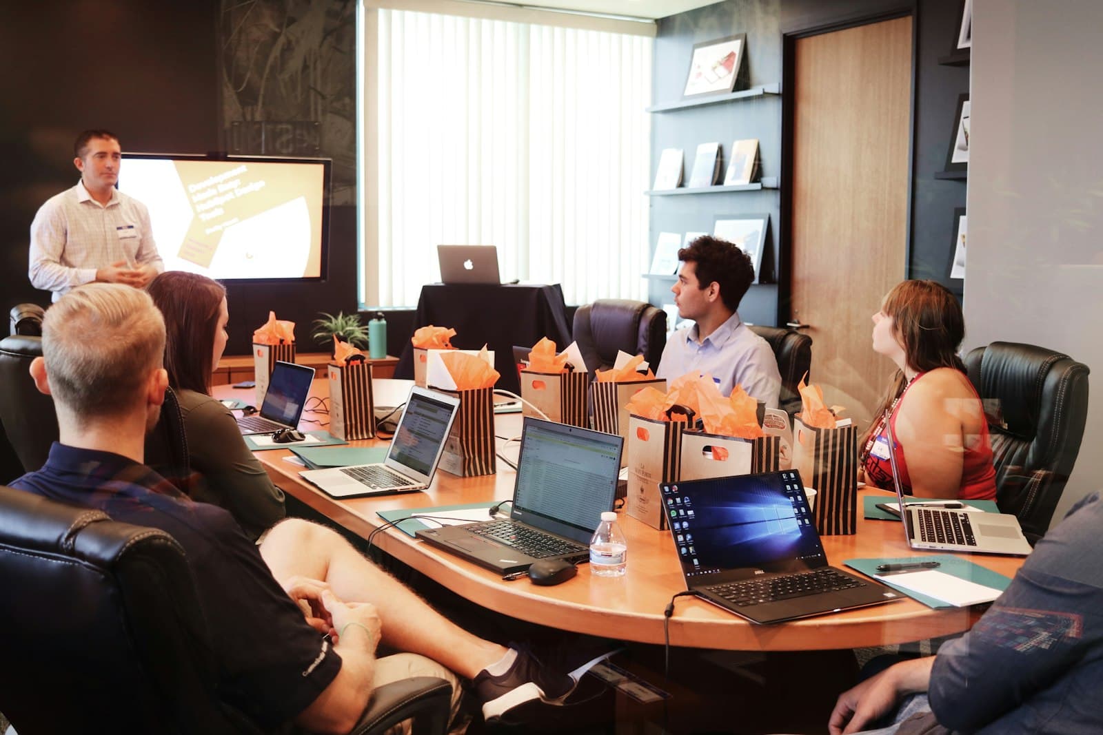 A facilitator presenting to a team around a boardroom table with laptops open
